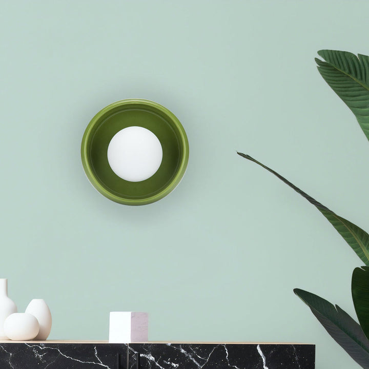 Grüne Wandleuchte mit rundem Design auf mintgrüner Wand, moderne Innenbeleuchtung.