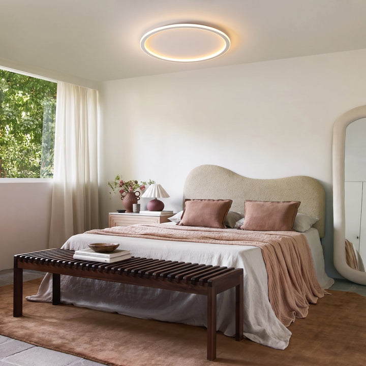 Ringleuchte über einem modernen Schlafzimmer mit geschwungenem Kopfteil, rosa Decke, Holzbank und Spiegel. 11