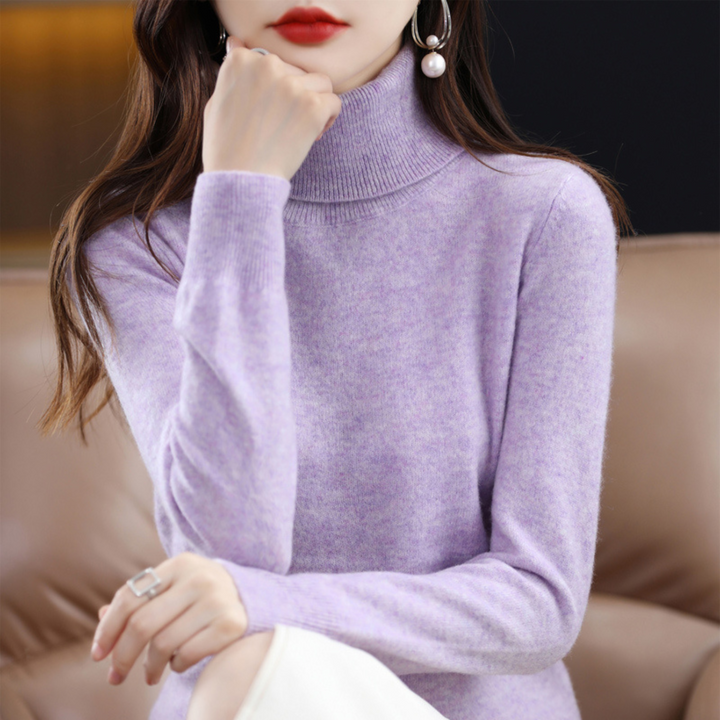 Fliederfarbener, melierter Rollkragenpullover am Model, die Hand ans Kinn gelegt, dazu eine weiße Hose. 6