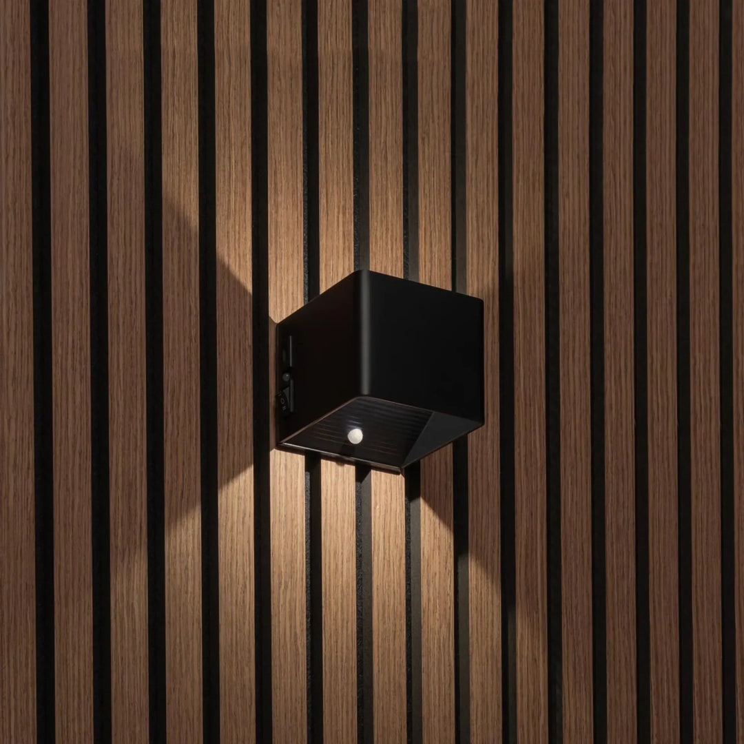 Schwarze würfelförmige Wandleuchte an Holzlamellenwand, Schalter an der Seite, Bewegungsmelder an der Unterseite sichtbar 1