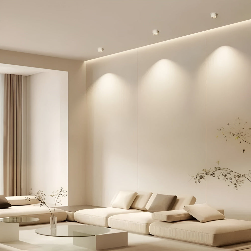 Weiße Einbaustrahler in der Decke eines hellen Wohnzimmers beleuchten die Wand über einem beigen Sofa 2