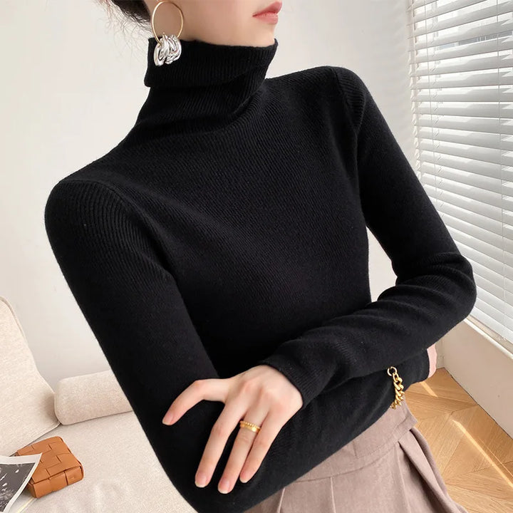 Schwarzer Rollkragenpullover am Model, Arme verschränkt, kombiniert mit beigem Faltenrock und goldenem Ring 8