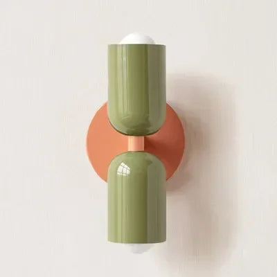 Wandlampe mit olivgrünen Schirmen und einer runden lachsfarbenen Wandplatte, vor heller Wand fotografiert. 21