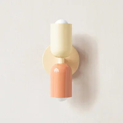 Wandlampe mit cremefarbenem oberem Schirm, cremefarbener Wandplatte und lachsfarbenem unterem Schirm vor heller Wand. 16